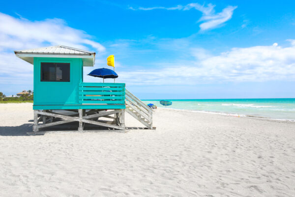 Photo of life guard shack and white sandy beach with crystal blue ocean water.