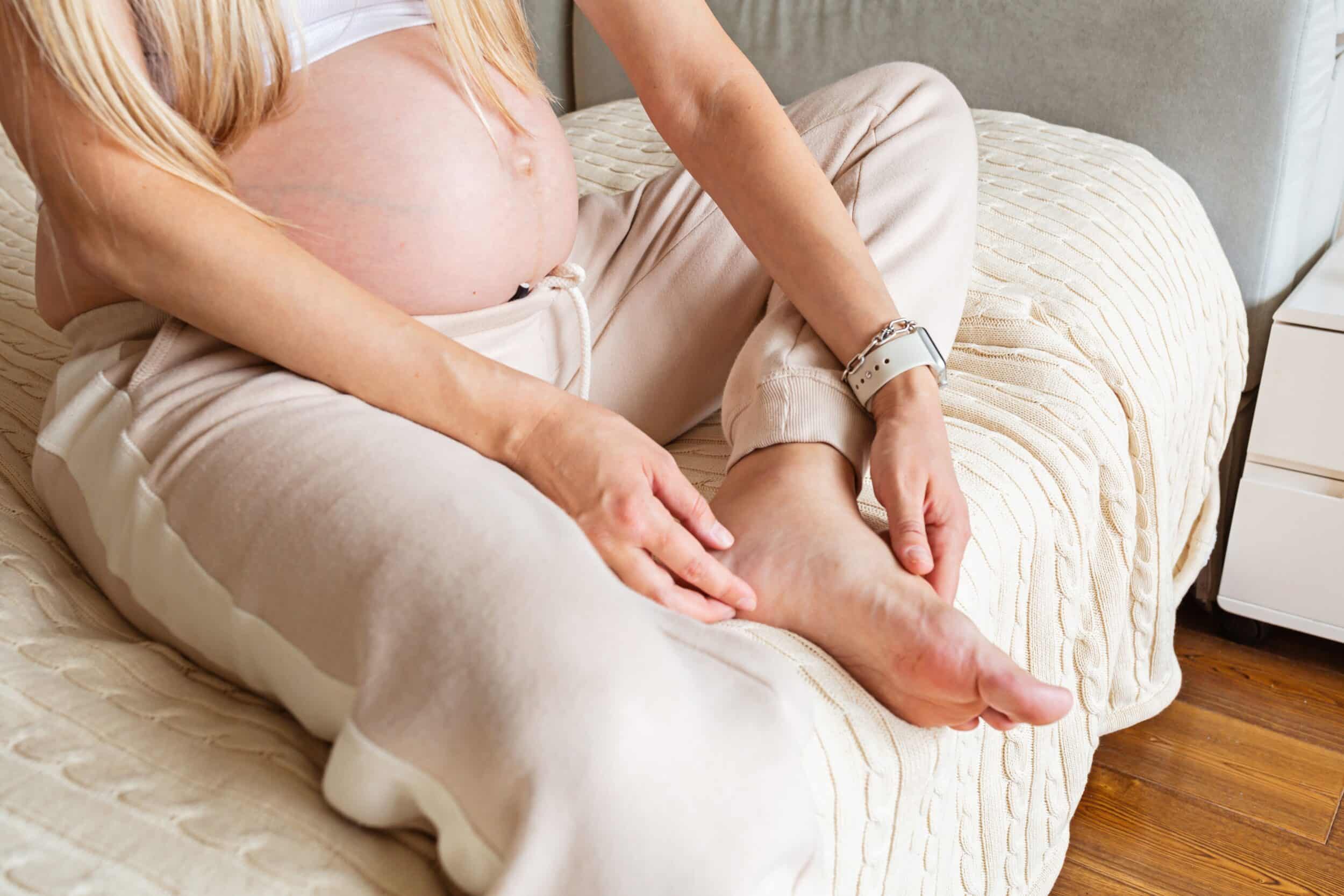 Pregnant woman sitting on a bed holding her legs due to varicose veins in Tampa